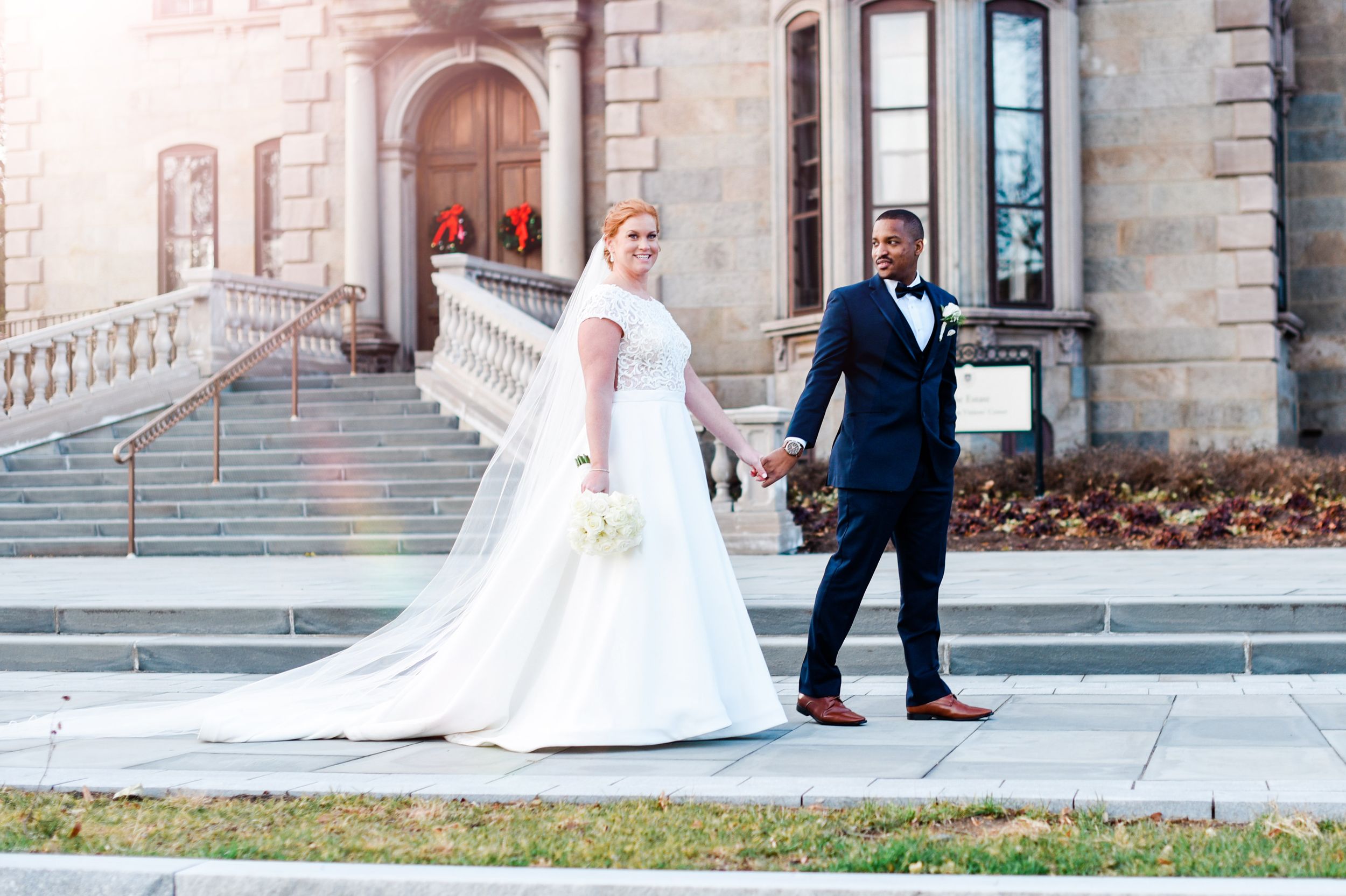 A wedding couple photographed from behind walking along classic stone architecture.