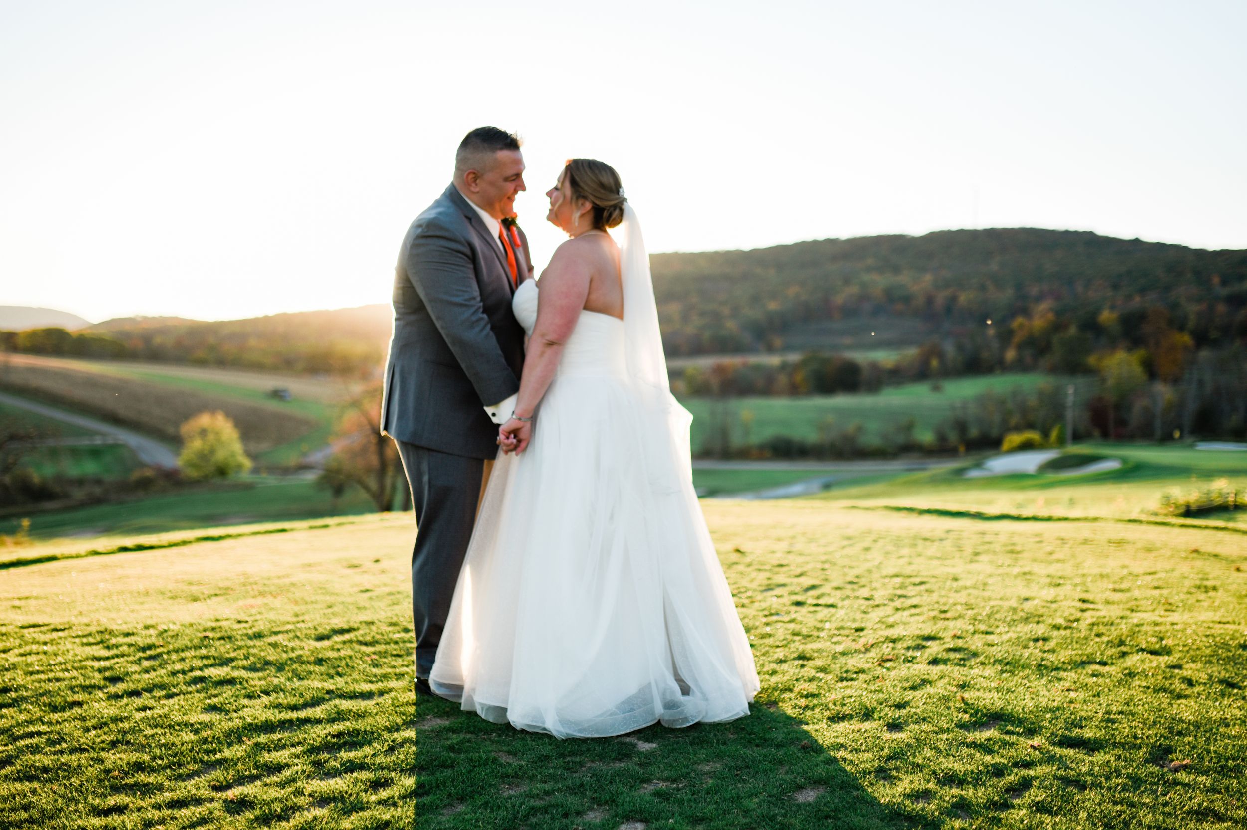 Wedding couple embracing in golden sunlit field during sunset.