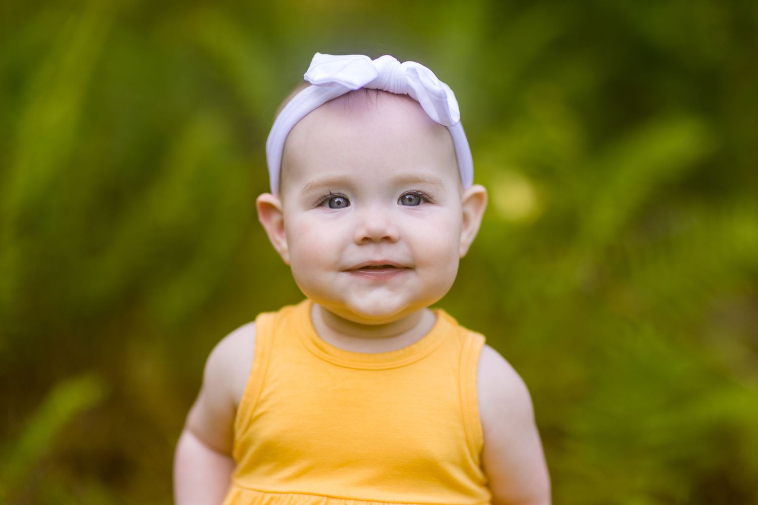 Close-up portrait of baby in bright yellow dress with white bow headband.