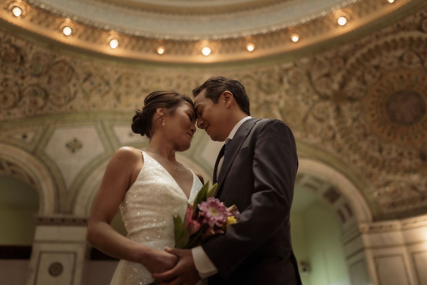 A couple shares an intimate moment under ornate ceiling architecture with string lights.