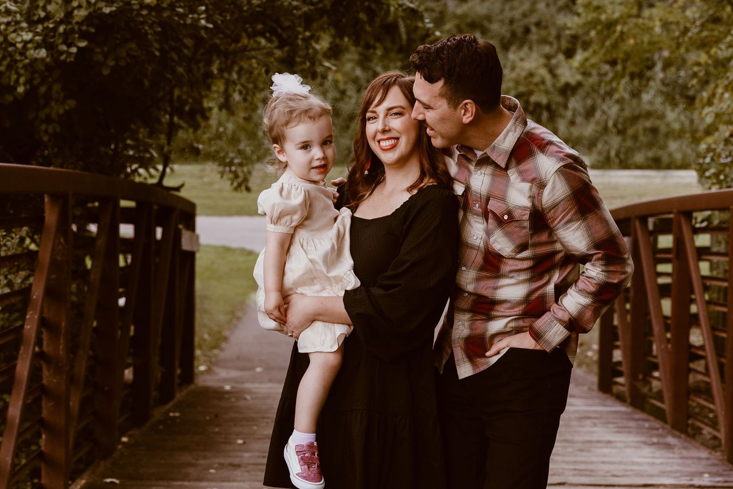 A family shares a joyful moment together while posing on a wooden bridge in nature.
