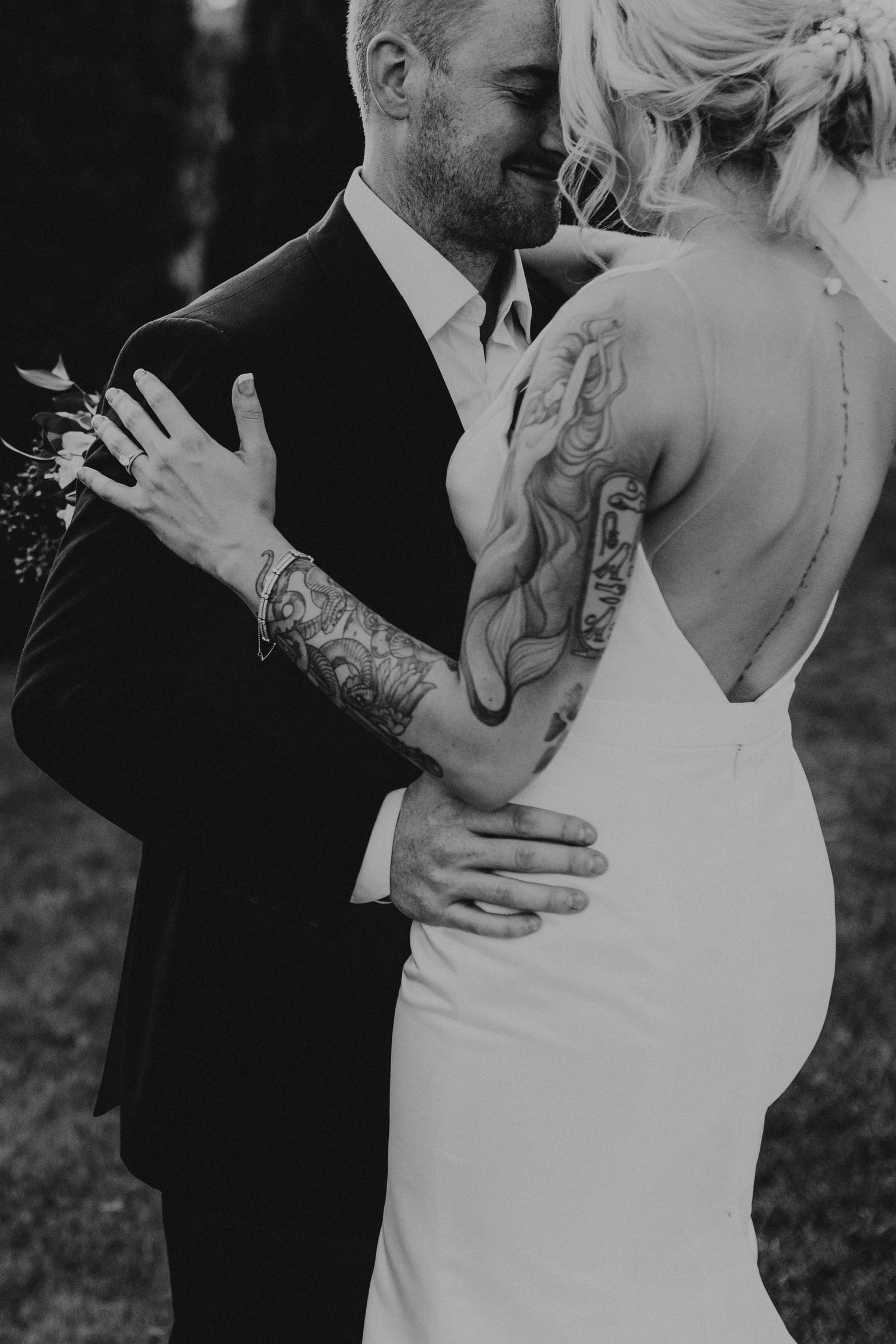 Black and white wedding portrait showing intimate embrace and bride's tattooed arm.