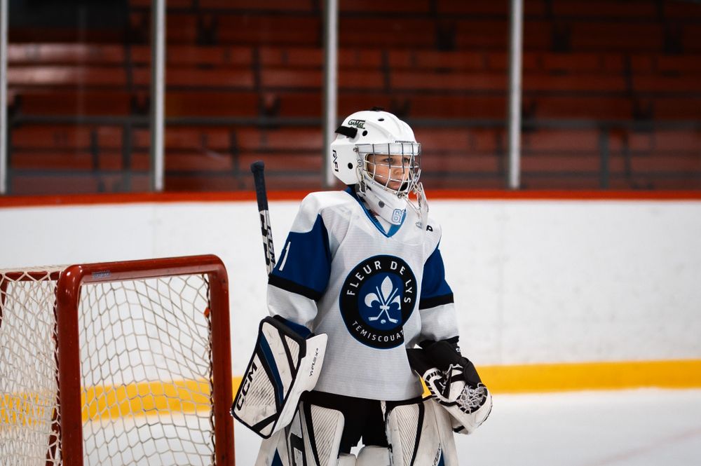 Youth hockey goalie in white jersey standing ready at the net.