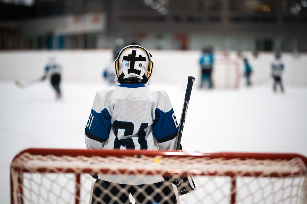 Hockey goalie in white jersey number 64 standing at net.