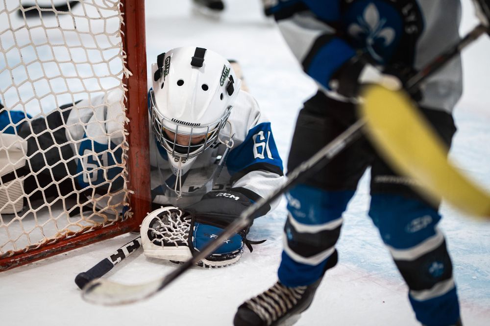 Hockey goalie making save at ice rink with blue player in frame.