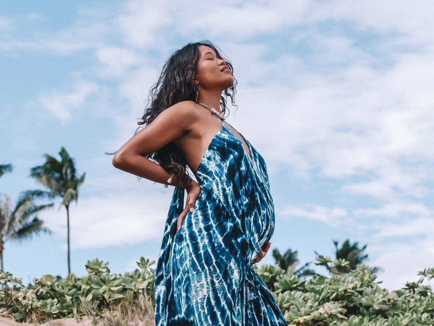 Woman in blue tie-dye dress posing gracefully against tropical backdrop.