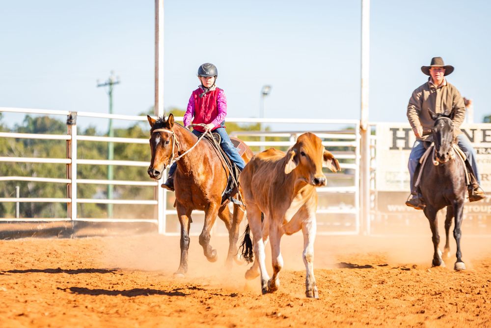 Riders practicing calf roping skills in dusty rodeo arena.