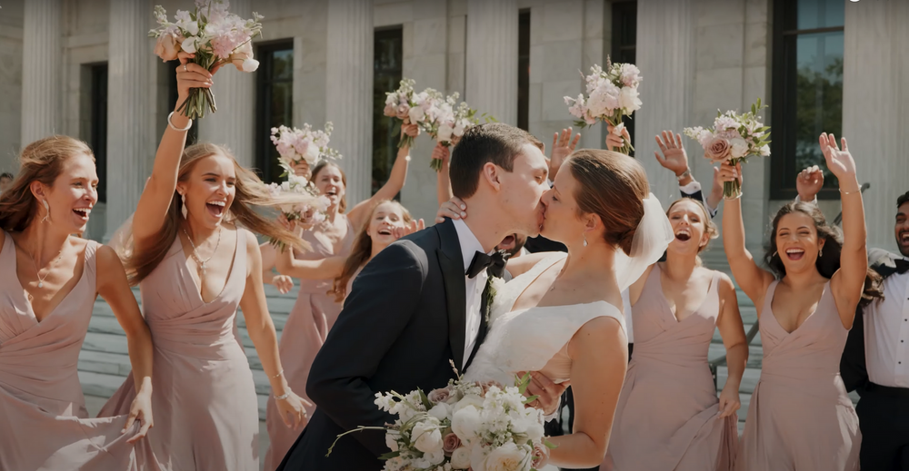 Wedding party cheers with bridesmaids in pink dresses holding floral bouquets.