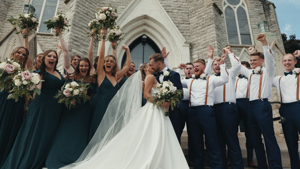 Wedding party celebrates outside historic church with bridesmaids in teal and groomsmen in navy.