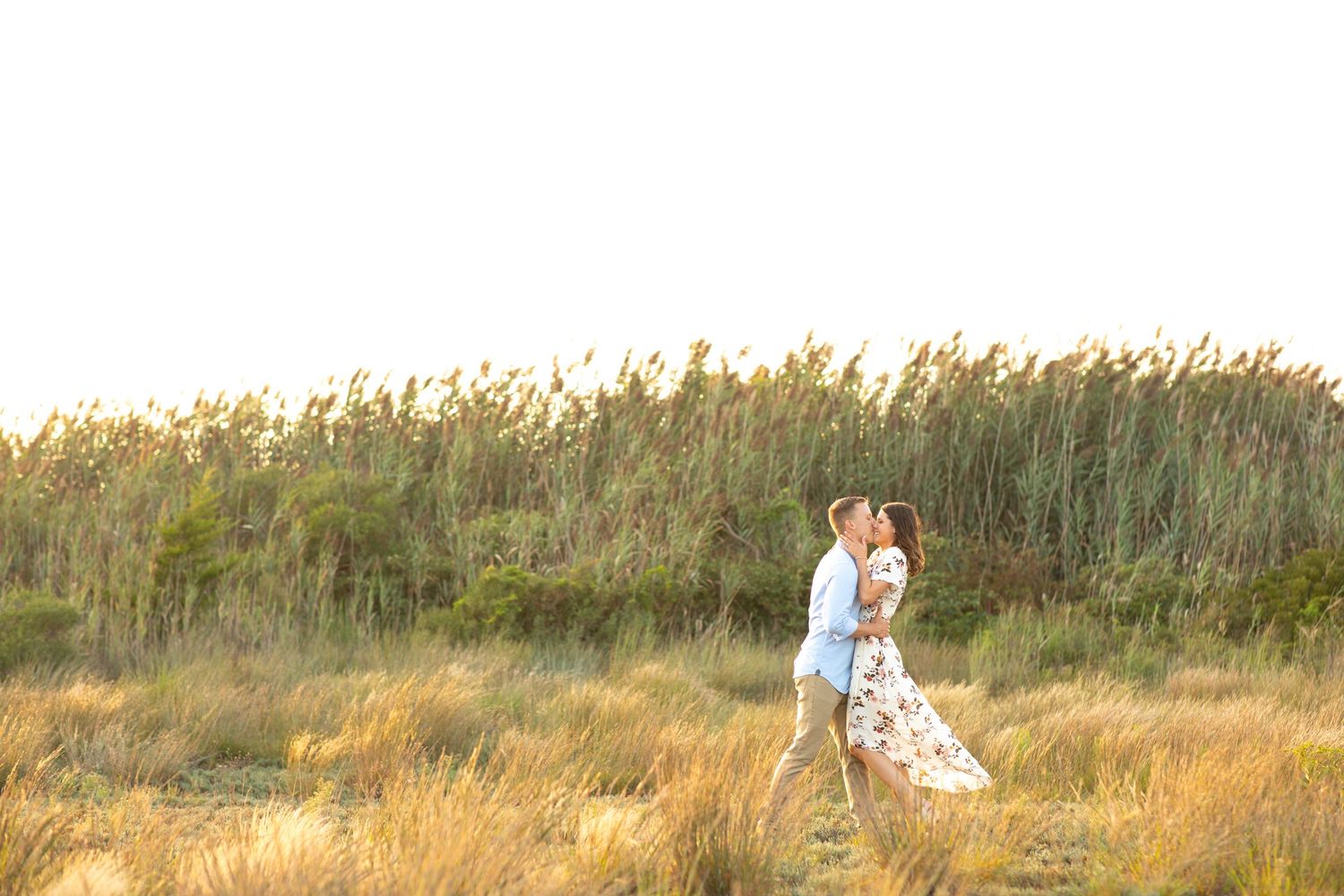 A romantic couple walking through tall grass at golden hour.