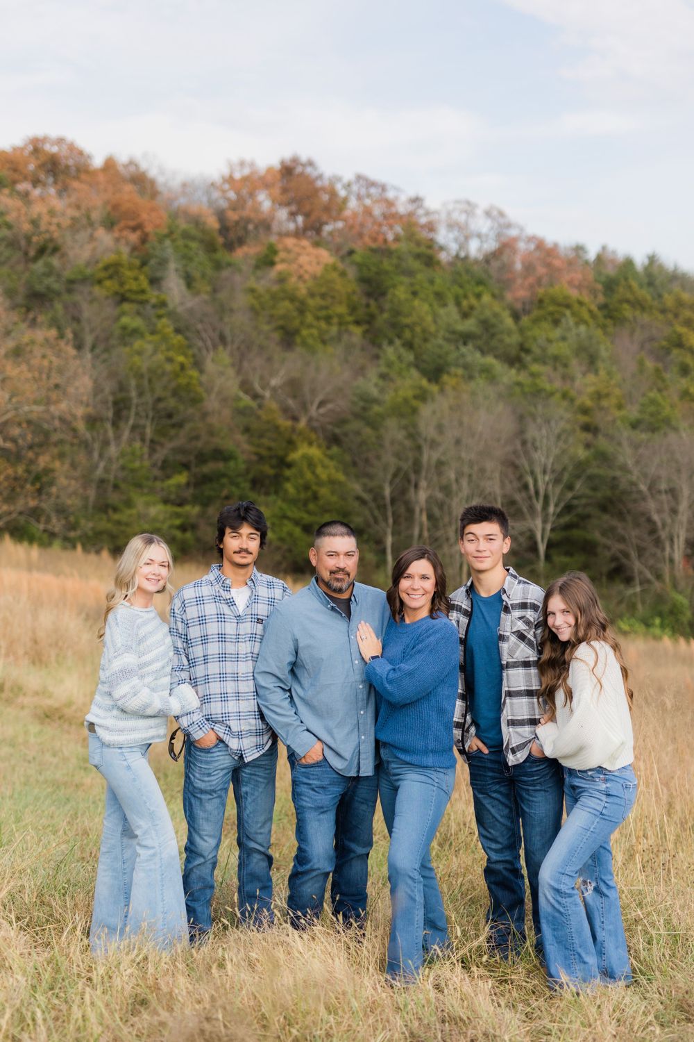 Family group wearing coordinated blue and plaid outfits poses in autumn field setting.