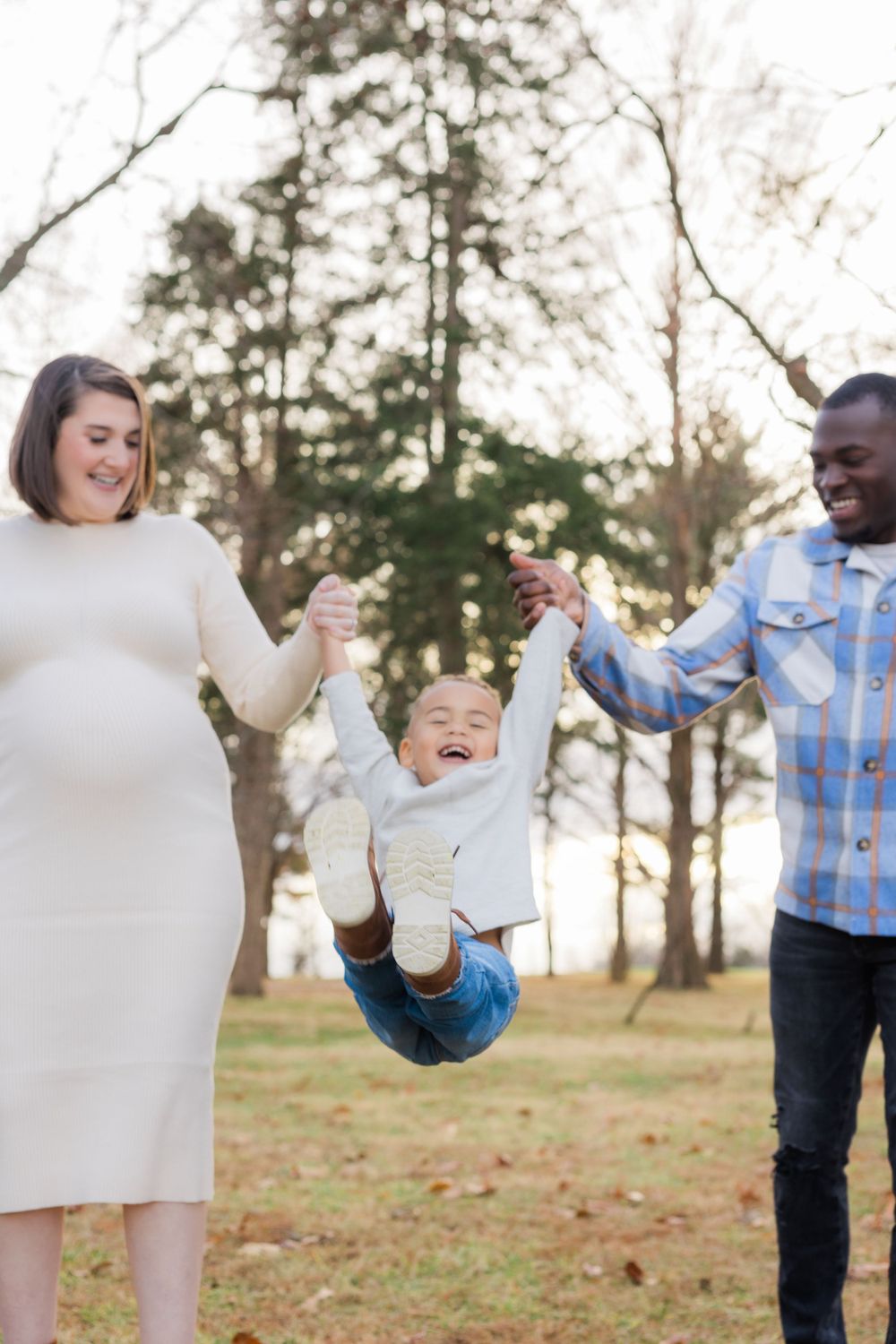 Family swinging child in the air while laughing together in a forest setting.