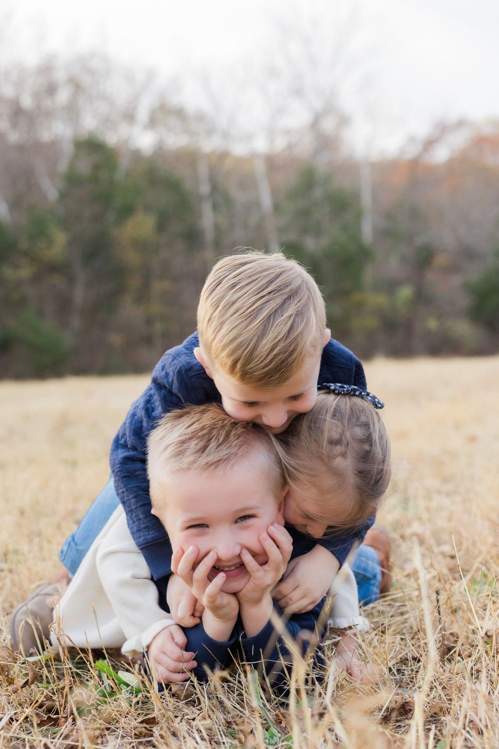 Three playful siblings huddled together while playing in a grassy autumn field.