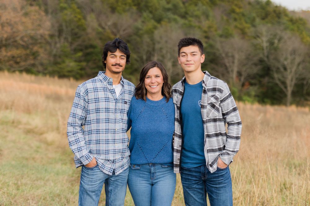 Three family members in casual attire pose together in a golden autumn field.