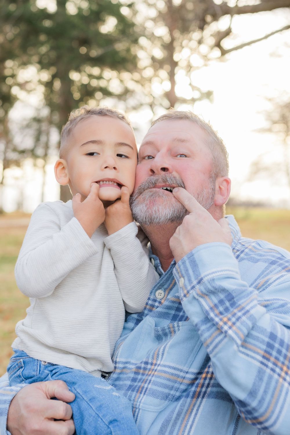 Playful portrait of two generations making silly faces together outdoors.