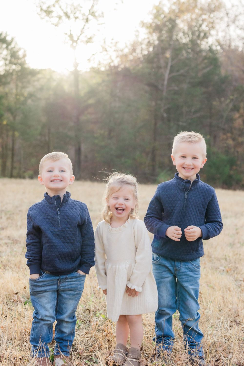 Three siblings standing in a field wearing coordinated outfits of navy and beige.