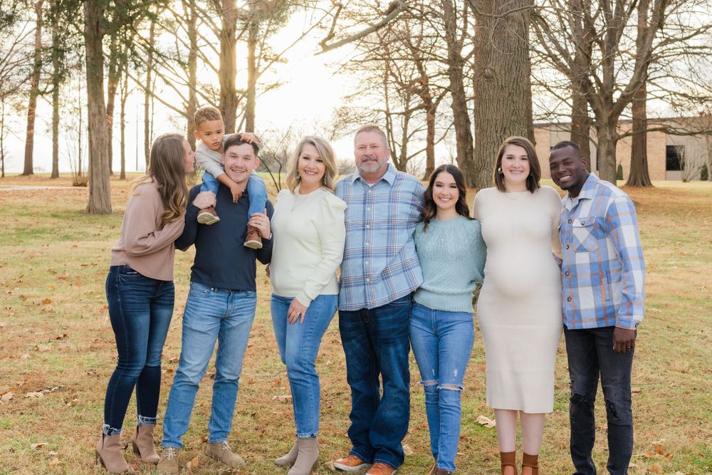 Extended family group posing together for a portrait in a wooded setting at sunset.