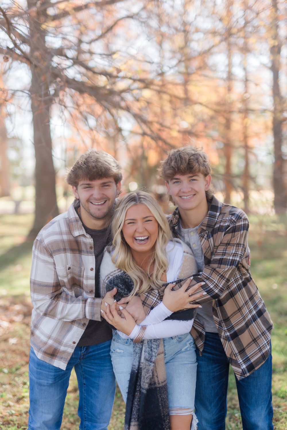 Group of siblings sharing joyful laughter while embracing outdoors in autumn setting.