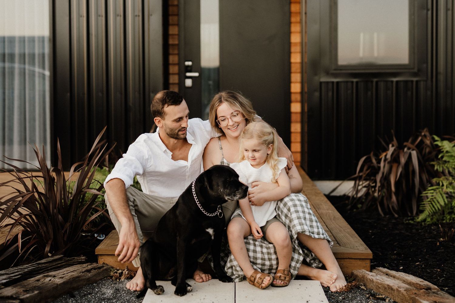 Family sits on porch with their black dog for casual outdoor portrait.