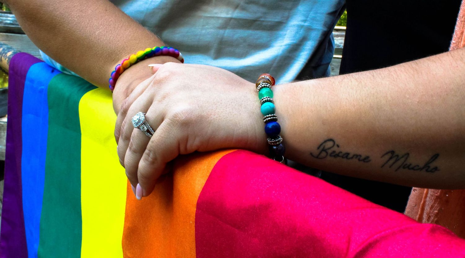 Close up of hands with jewelry against rainbow pride flag fabric.