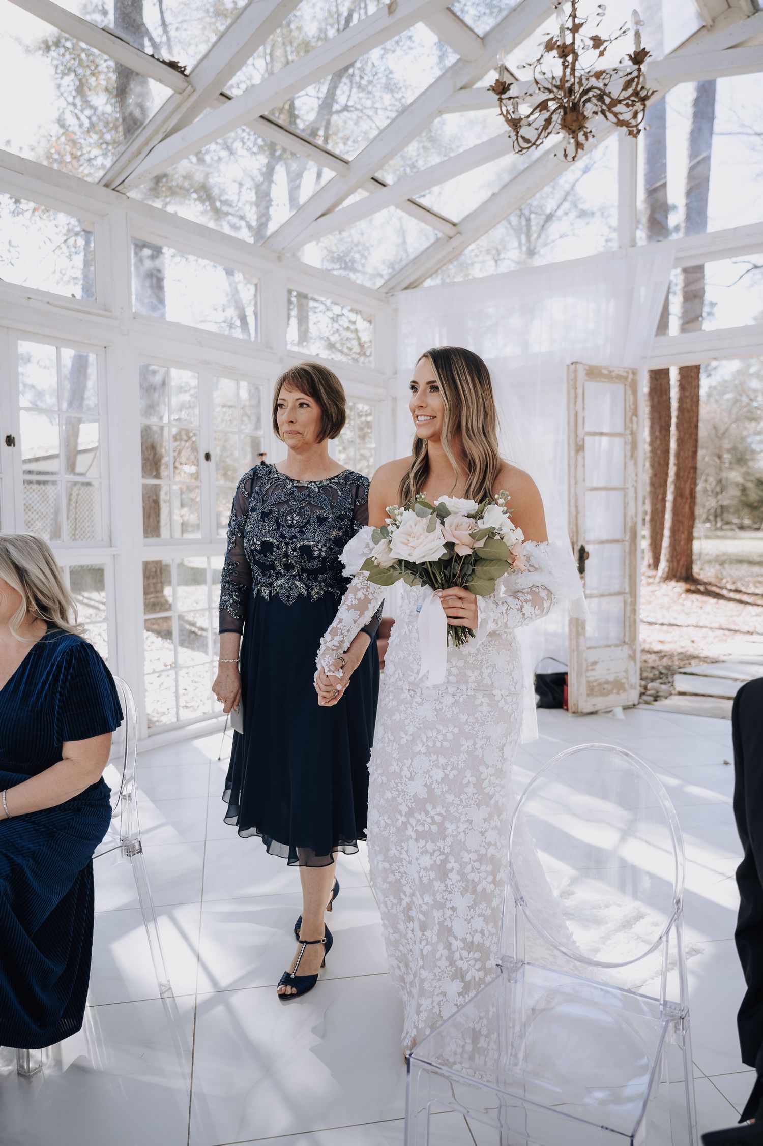 A timeless wedding moment captured in a sunlit conservatory with elegant chandelier.