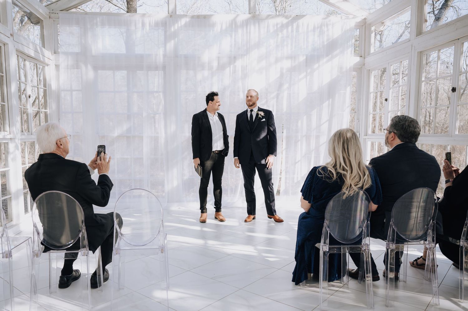 A small intimate ceremony in a bright conservatory-style room with white drapes.