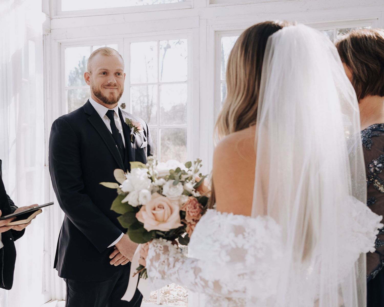 A tender moment during a wedding ceremony in a light-filled glass room.