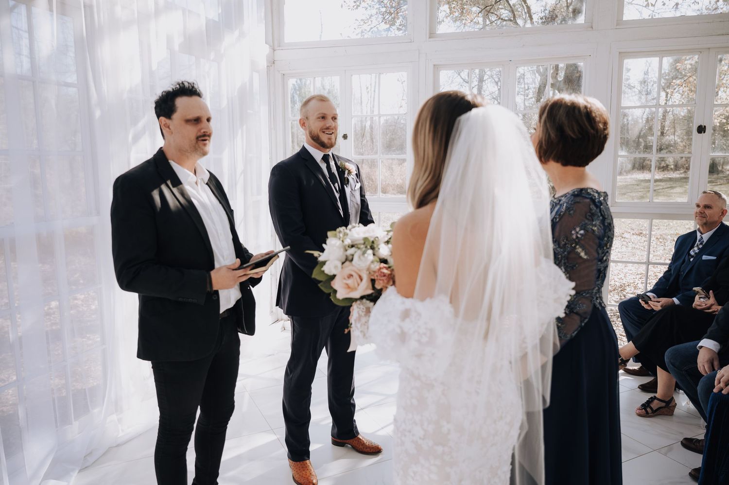 An intimate wedding ceremony taking place in a bright, glass-enclosed space.