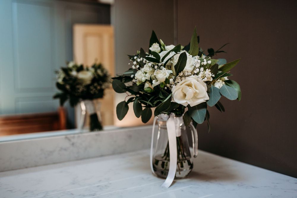 A wedding bouquet of white roses and eucalyptus leaves in a glass vase.