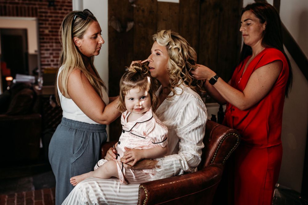 Wedding preparation scene with hair and makeup styling in a rustic brick-walled room.