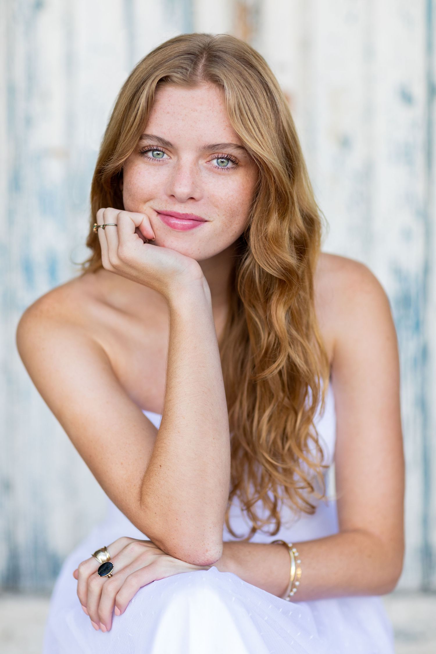 A high school senior of woman in white top with flowing hair against rustic background.