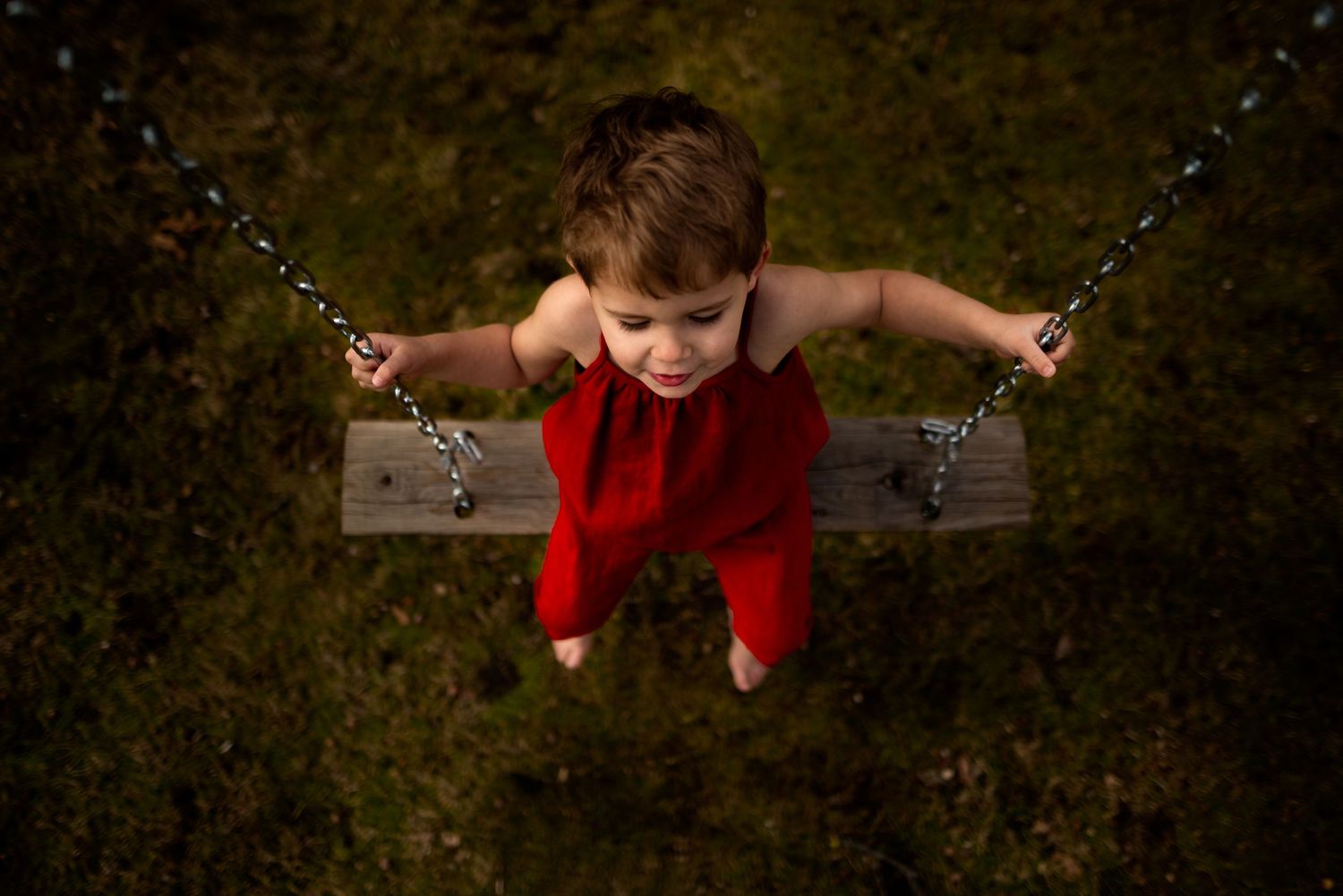 A child in red clothing swings joyfully outdoors.