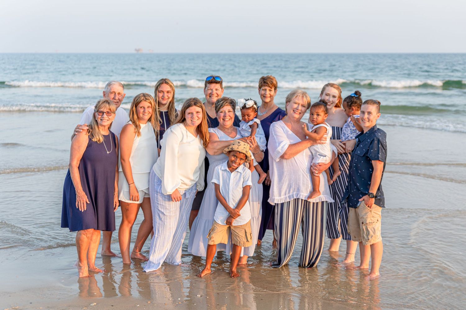 Extended family gathers for beach portrait wearing coordinated coastal colors.