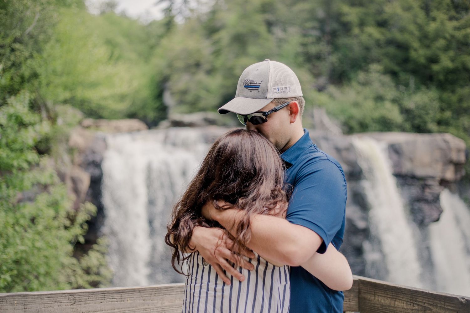 A couple's engagement moment captured on a scenic overlook with a cascading waterfall in the background.
