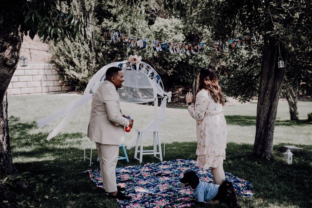 Man in tan suit presenting a surprise proposal setup to woman in floral dress in a garden setting.