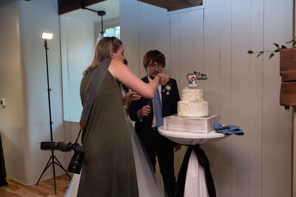 Wedding guests help serve slices of a white tiered cake at an indoor reception.