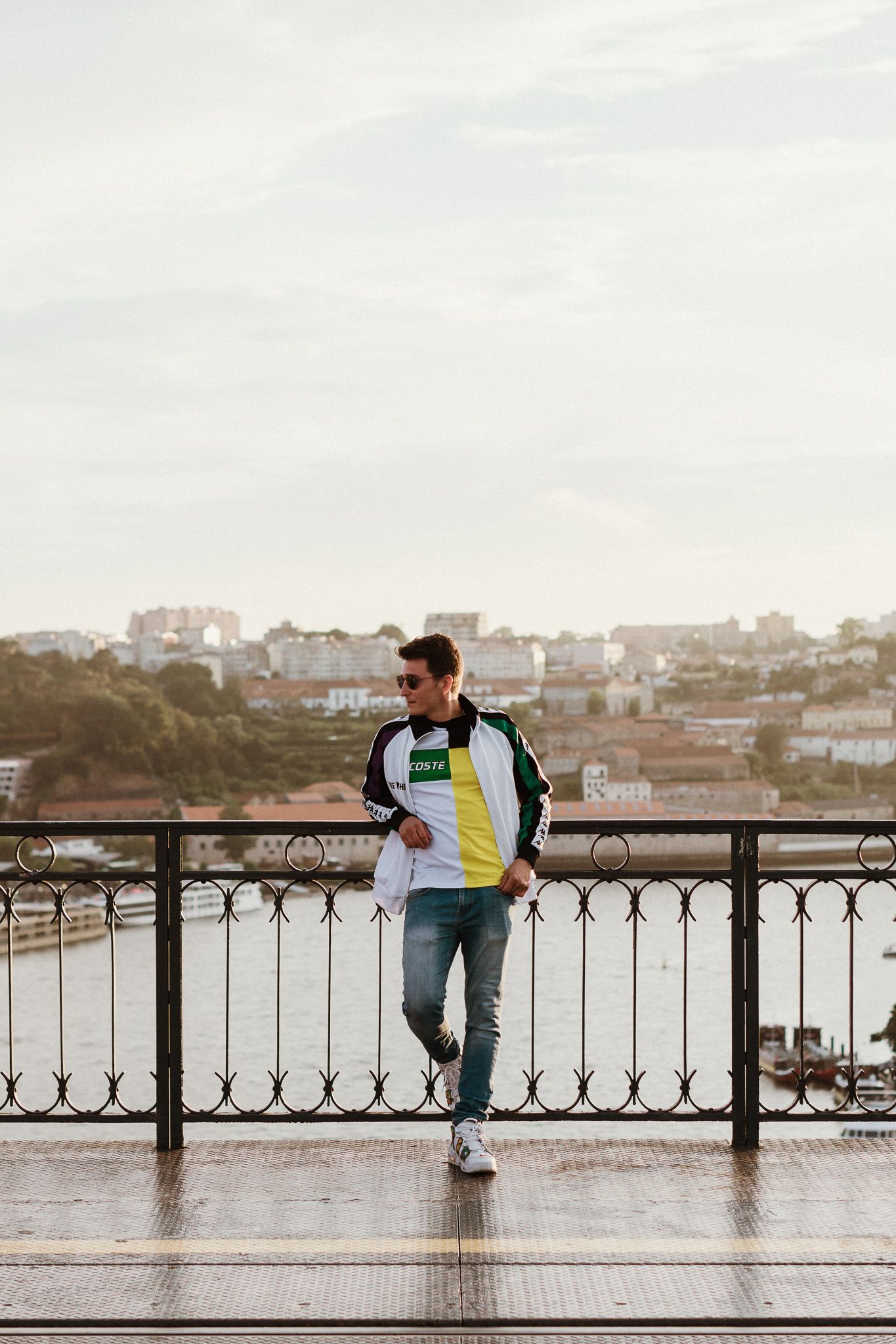 Person in casual wear standing on a wet bridge overlooking a coastal cityscape.