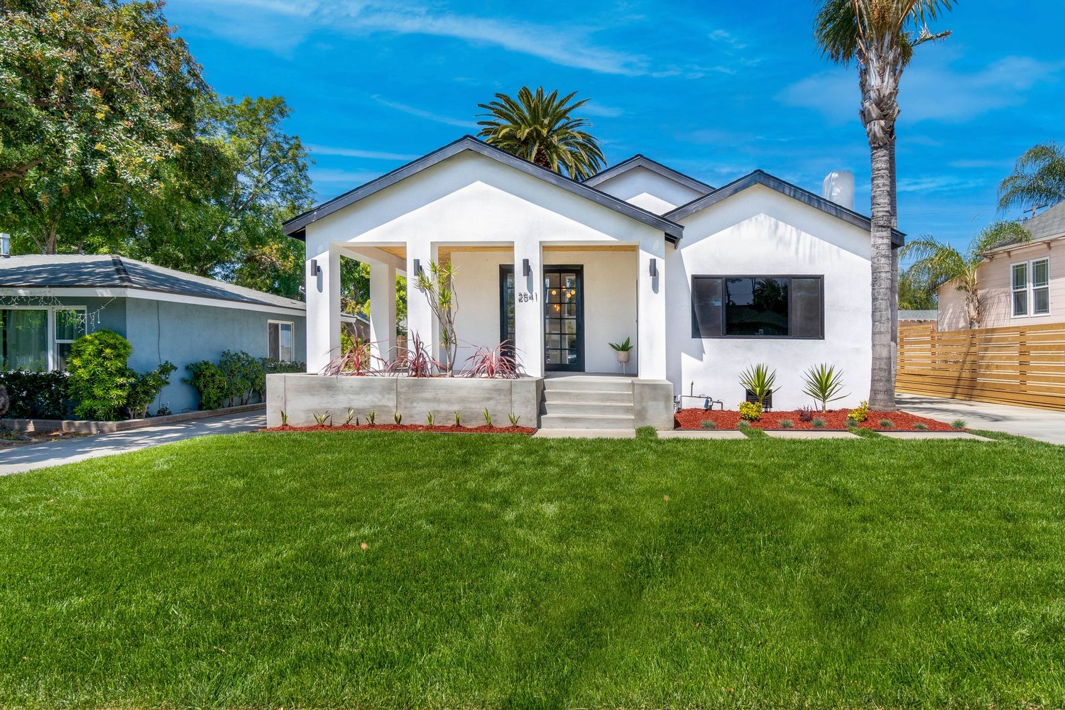 Modern white craftsman style house with columns and front porch features lush green lawn and palm tree in Jacksonville.