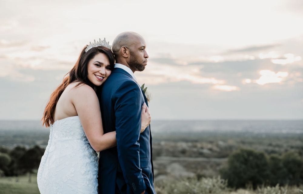 A newlywed couple embraces on a hilltop during golden hour.