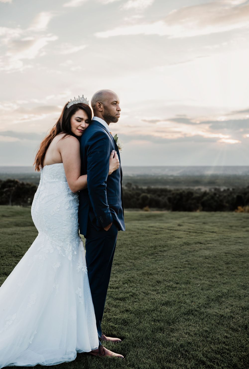 A romantic wedding portrait on a hilltop with dramatic sunset sky in the background.