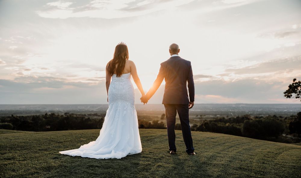 Romantic silhouette of newlyweds holding hands while enjoying sunset view from hilltop.