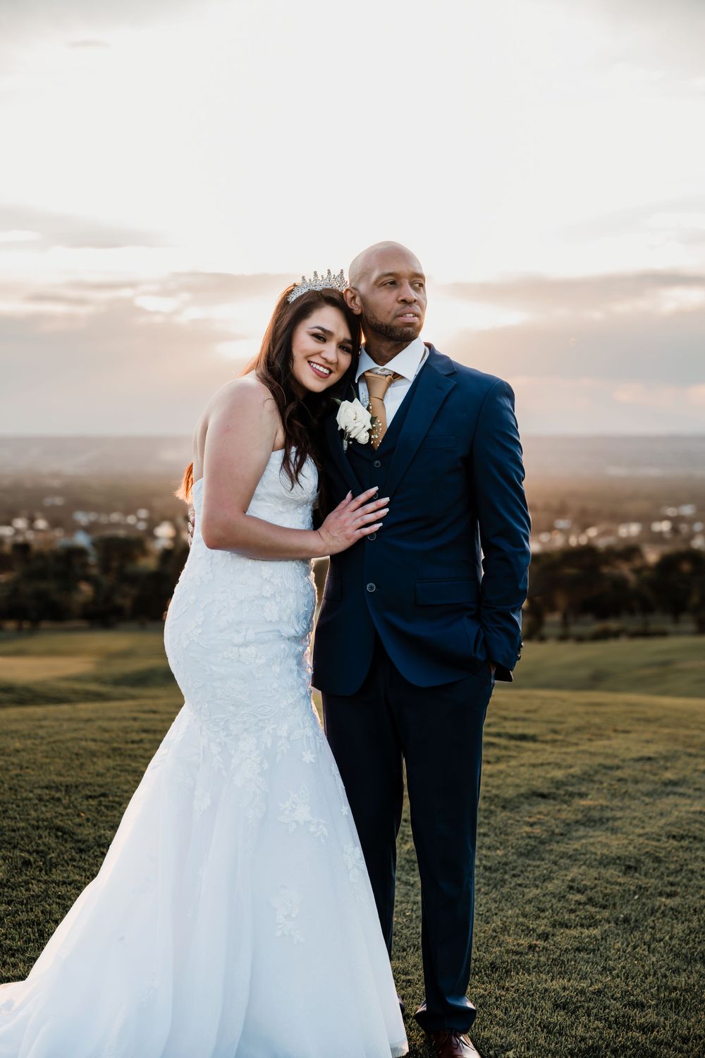 Joyful wedding portrait of couple embracing on hilltop during sunset.