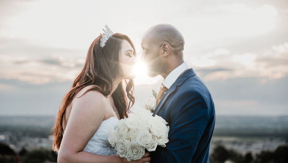 A romantic wedding couple shares an intimate moment at sunset with white bouquet.