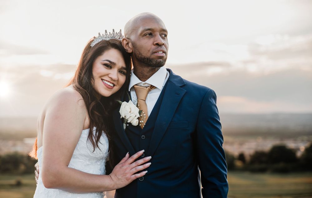 Newlywed couple in formal attire pose together during golden hour on scenic overlook.