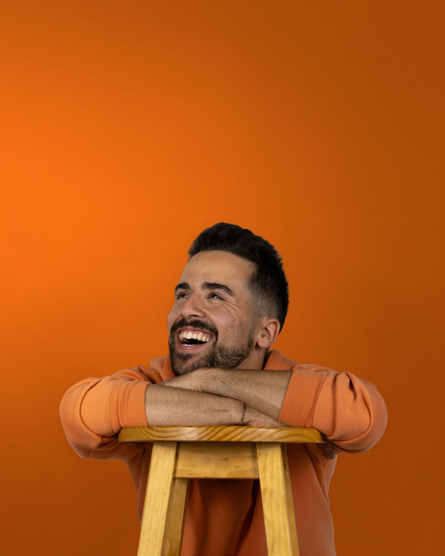 Person resting head on wooden stool against vibrant orange background showing various expressions.
