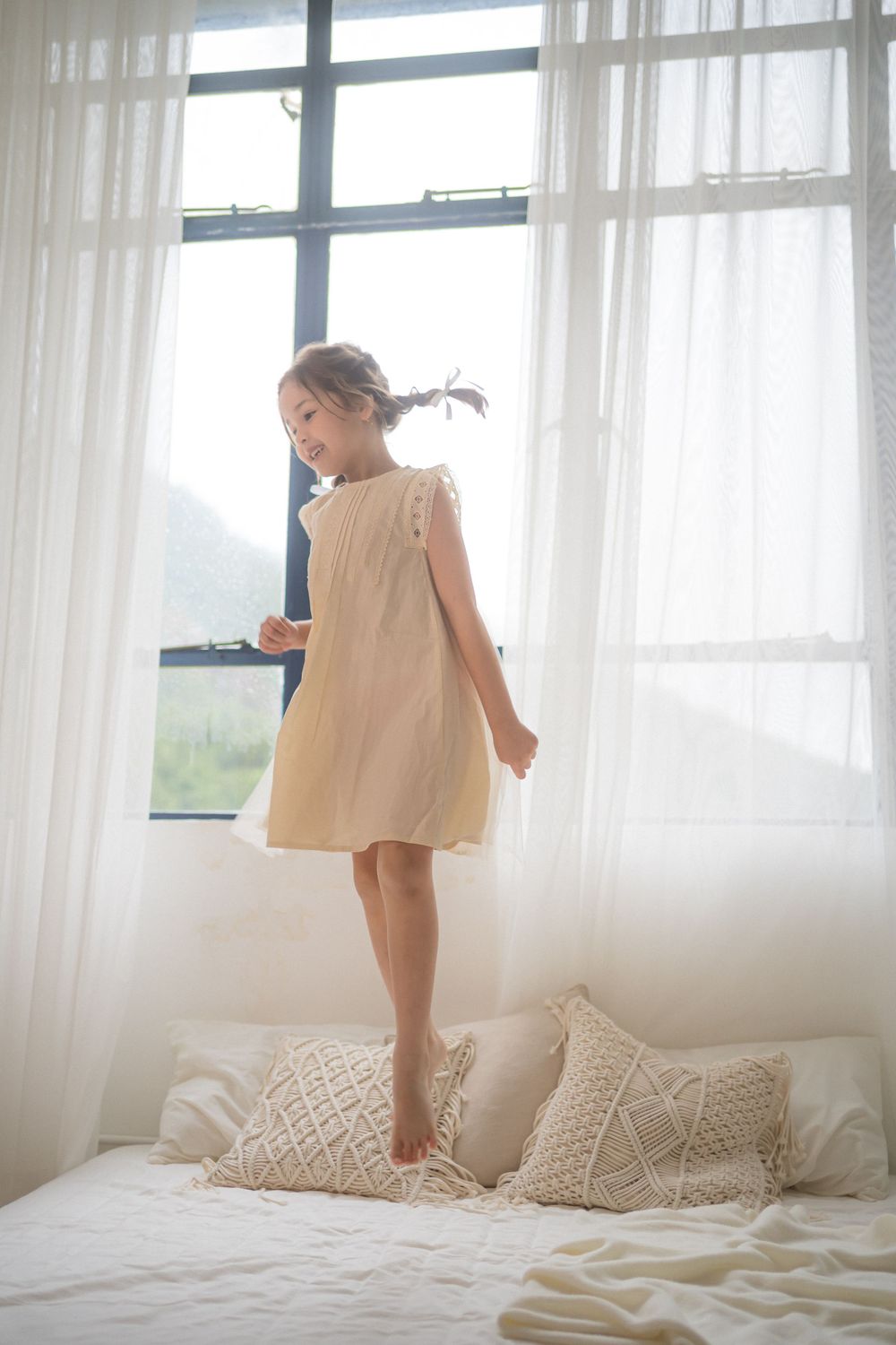 Light and airy scene showing playful moments on a white bed by a window.