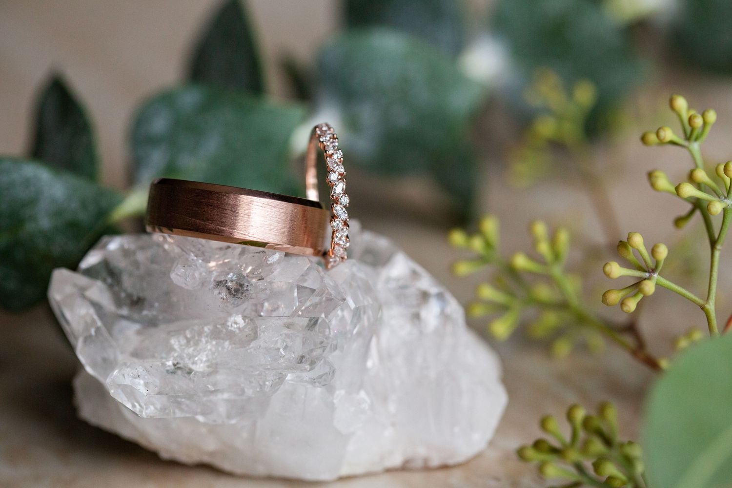 Rose gold wedding band and diamond ring resting on a crystal with greenery.