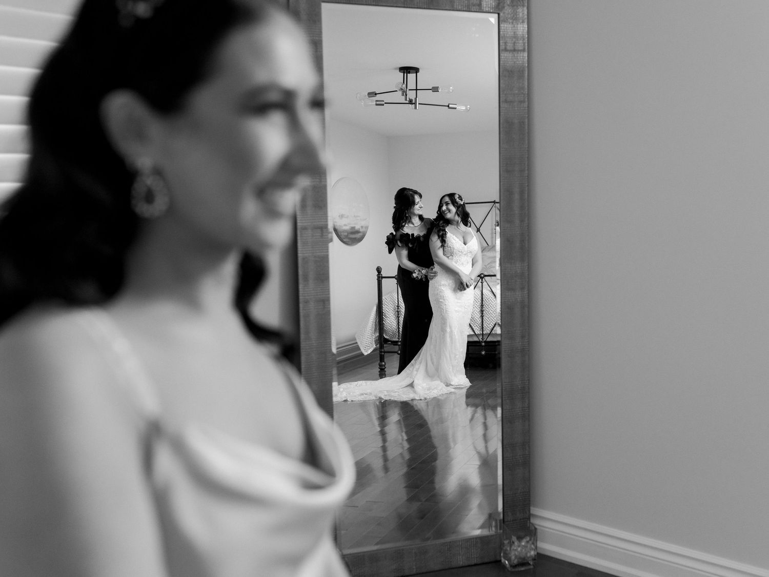 A photo of a mirror behind a bridesmaid, the reflection of the bride and her mother can be seen. Photo by Katie Crane.