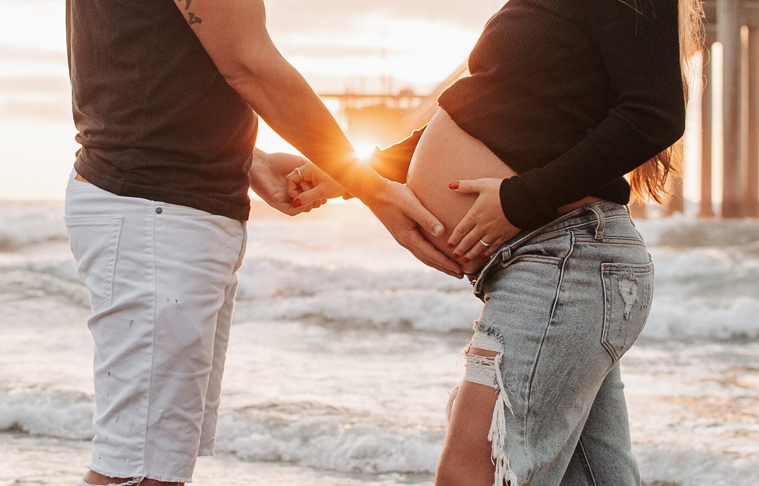A couple holding hands at sunset with golden light shining through, showing just their midsections in casual wear.