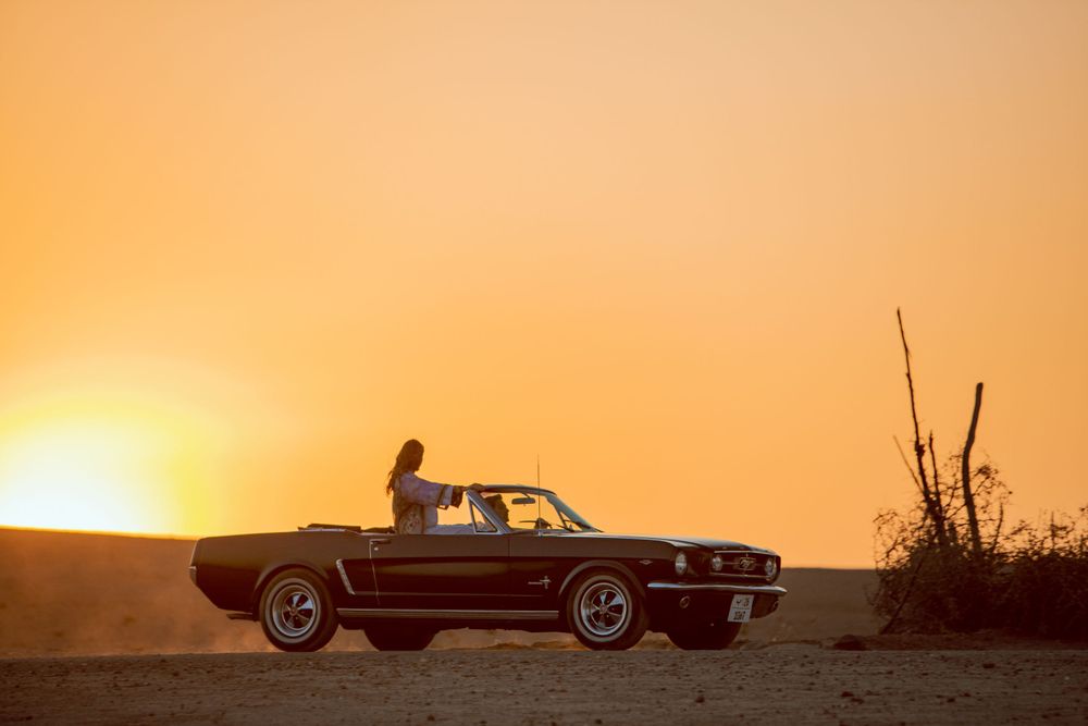 Classic Ford Mustang convertible silhouetted against a golden sunset on a hilltop.